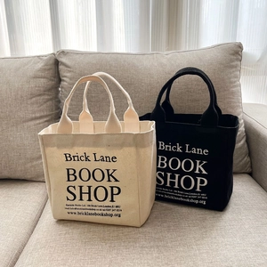 Minimalist Brick Lane canvas tote bags in cream and black on a grey sofa