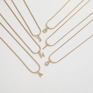 Detail of gold snake bone necklaces with crystal-encrusted letters A, D, G, H, J, T