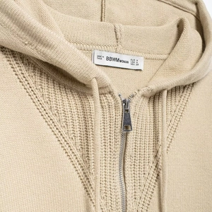 Beige knit hooded zip-up sweatshirt with detailed stitch texture and collar label