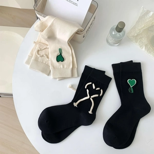 Dettaglio calzini in cotone con ricamo a cuore verde e design con lacci e nappe decorative