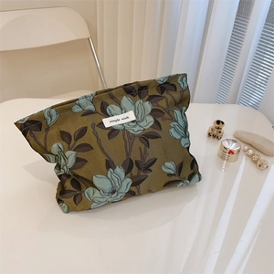 Detail of olive green jacquard floral makeup bag with simple wish label on white table