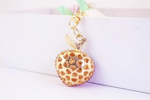Detail of a golden apple keychain with hollow heart patterns and red rhinestones