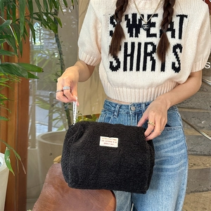 Detail of a large black faux shearling cosmetic bag with minimalist label and zipper pull