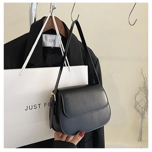 Detail of a minimalist black leather crossbody bag with elegant gold hardware buckles