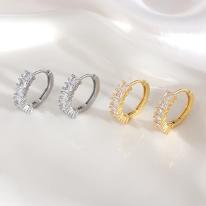 Elegant gold and silver huggie earrings with cubic zirconia stones on white silk