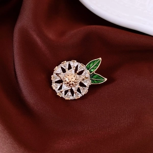 Macro detail of 14K gold plated flower brooch with cubic zirconia and green enamel leaves