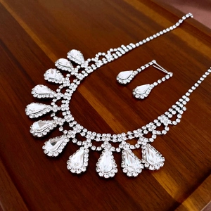Detailed close-up of a silver jewelry set with crystal waterdrop tassels on dark wood