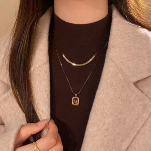 Detail of 18k gold plated layered necklace with brown oval stone on a brown sweater