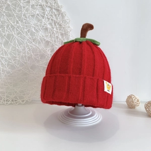 Close-up of red apple-shaped baby knit hat with green leaf and small boy label