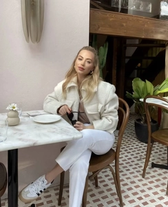 Detail view of white wool jacket texture and zipper on a seated model in a cafe