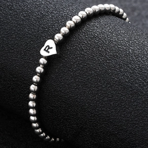 Macro detail of silver beaded heart charm bracelet with engraved letter R on leather