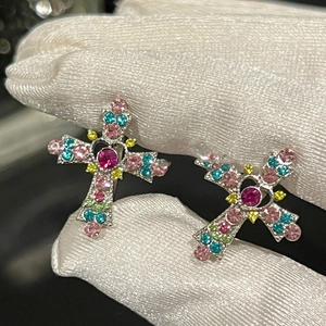 Detailed macro view of silver cross earrings with multicolor rhinestones held by a hand