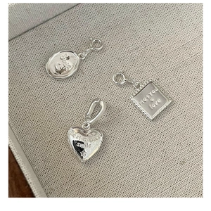Macro view of silver S925 charms with engraved smile and heart patterns on beige texture