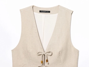 Détail d'un gilet en lin beige montrant la texture du tissu et les perles en bois