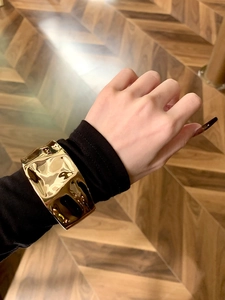 Nahaufnahme eines breiten goldenen Armreifs mit Hammerschlag-Struktur über schwarzem Ärmel