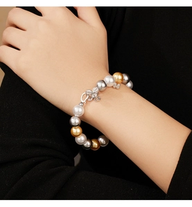 Detailed close-up of mixed color pearl bracelet with clover pendant on model's wrist