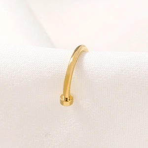 Close-up of golden U-shaped stainless steel nose ring on white textured fabric