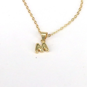Detailed view of a golden bubble M initial pendant necklace on a clean white background