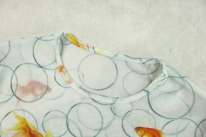 Detail of round neckline with goldfish print and fine stitching on a printed dress