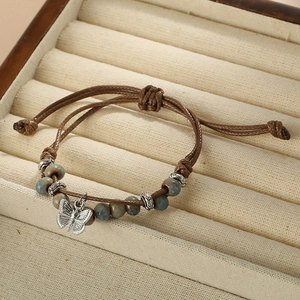 Detail of woven rope bracelet with ceramic beads and silver butterfly charm