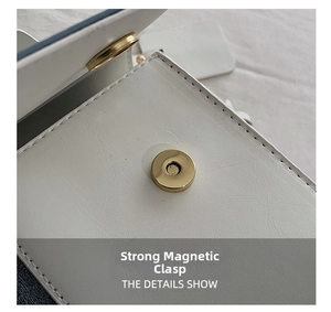 Detail view of white leather crossbody bag featuring a strong gold magnetic buckle closure