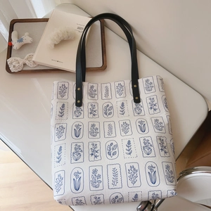 Minimalist canvas tote bag with vintage blue floral patterns and black leather handles