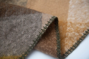 Close-up of wool-blend plaid scarf showing textured brown checks and green stitching