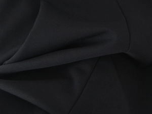 Dettaglio del tessuto nero di un abito a collo alto con un drappeggio morbido ed elegante