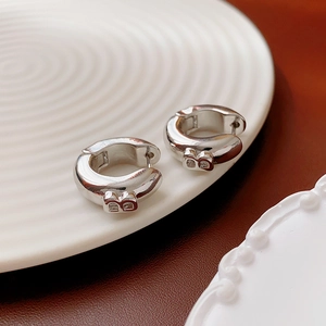 Close-up of silver chunky hoop earrings with letter B charm on white textured tray