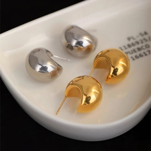 Macro detail of minimalist gold and silver ball stud earrings on a ceramic tray