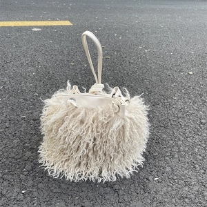 Top-down view of a creamy white faux lamb wool drawstring bucket bag on an asphalt surface