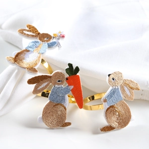 Detailed view of three embroidered rabbit napkin rings with golden metal accents