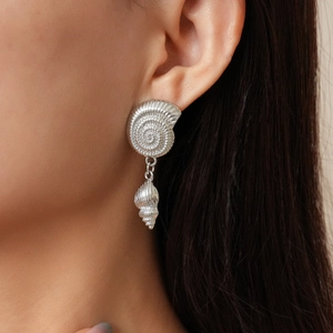 Close-up of silver conch and nautilus shell earrings worn by a model for a chic look