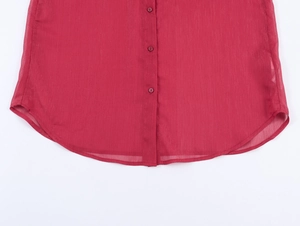Détail d'une chemise rouge en mousseline avec ourlet incurvé et fermeture boutonnée