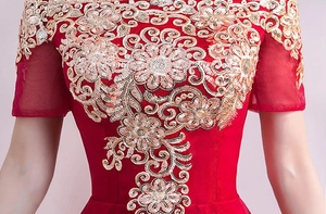 Dettaglio del ricamo floreale dorato e paillettes sulle spalle dell'abito rosso