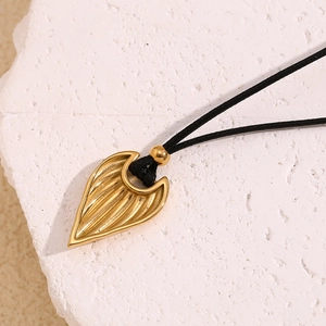 Macro shot of gold leaf heart pendant with textured stripes on black cord necklace
