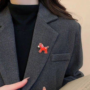 Detailed view of red resin horse brooch with gold trim on grey wool suit lapel