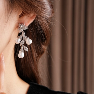 Détail de boucles d'oreilles feuille argentée avec perles blanches et zircons sur modèle