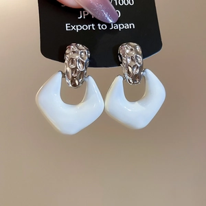 Detailed close-up of geometric white enamel earrings with hammered silver metal texture