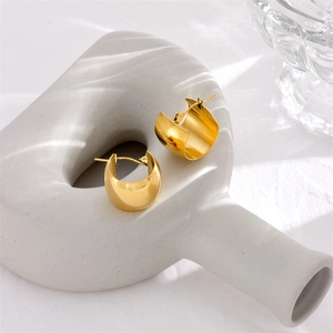 Modern thick gold circle earrings with polished finish on a white geometric prop