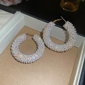 Close-up of gold-plated C-shaped hoop earrings with inlaid pearls and AB crystals