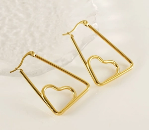 Close-up of gold heart-shaped titanium steel earrings on a glass tray with soft lighting