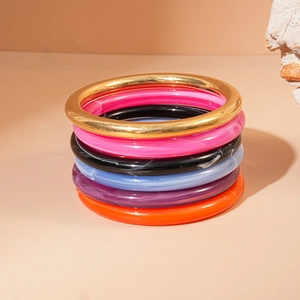 Gros plan de 6 joncs colorés en résine acrylique et bracelets en métal doré empilés