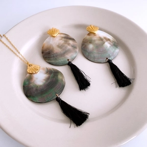 Detail of necklace and earrings set with shell pendants and black tassels on ceramic plate