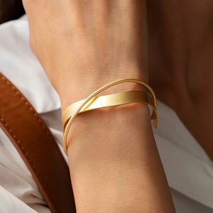 Detail of matte gold double-layer cross cuff bracelet on a model wearing white