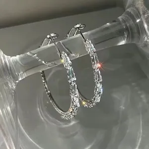 Detailed view of silver hoop earrings featuring baguette-cut zircon stones on a glass display