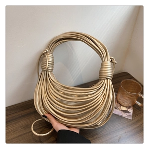 Detail of gold knot handle on a textured woven metallic shoulder bag on a wooden table
