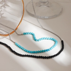 Minimalistische Stahlkette mit schwarzen Onyx-Perlen, als Herz geformt auf weißem Grund