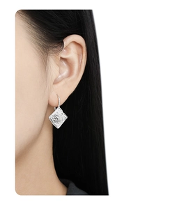 Close-up of geometric silver stud earrings with lava texture and crystals on ear model