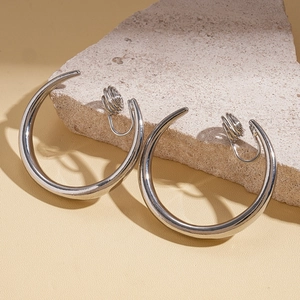 Silver geometric clip-on hoop earrings placed on a natural stone and beige surface